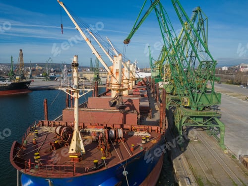 Preview: A bulk carrier ship loaded with grain is docked at a busy port, with workers and machinery seen in