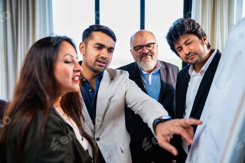 Preview: Indian Asian Corporate team discussing a strategy drawn on whiteboard by a young businesswoman