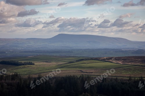 Preview: Scenic view of rolling green hills with a distant mountain under a partly cloudy sky in Skipton