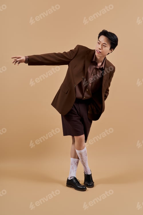 Preview: Elegant young man in a stylish brown blazer poses creatively in a studio setting