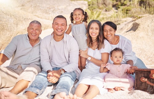 Preview: Portrait of a smiling mixed race family with little girls sitting together at the beach. Adorable
