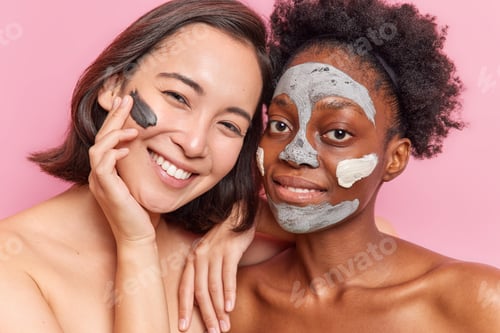 Preview: Two diverse women apply clay mask on face smile gladfully stand shirtless indoor have friendly relat