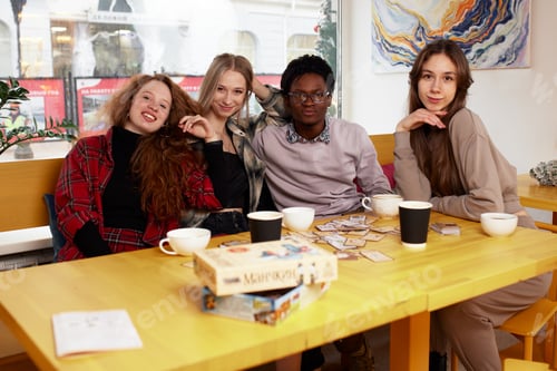 Preview: Mixed race happy young people gathering in cafe, sitting at table, chatting, talking, drinking