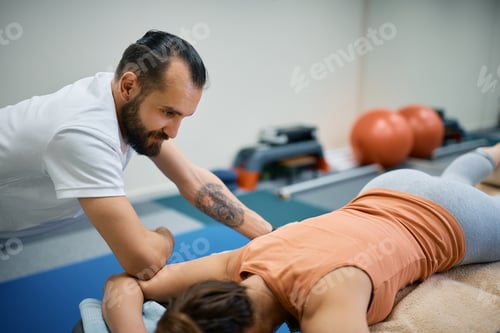 Preview: Male physical therapist giving sports massage to a woman at health club.