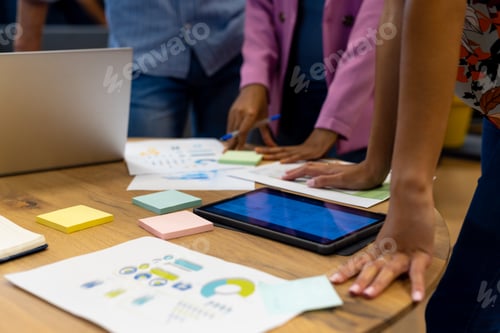Preview: Midsection of diverse colleagues in discussion using tablet and laptop in casual office meeting