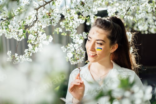 Preview: Outdoor portrait of ukrainian woman with blue and yellow ukrainian flag on her cheek on cherry