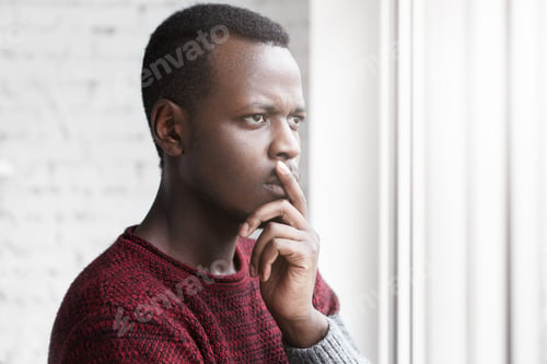 Preview: Half profile portrait of handsome young African American writer looking through window with pensive