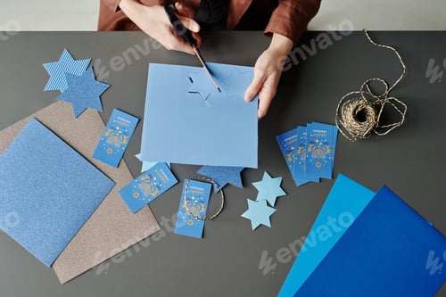 Preview: Above angle of hands of unrecognizable woman cutting out blue stars