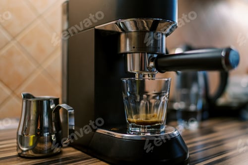 Preview: Black coffee drips into a glass on the tray of a carob coffee machine on a table