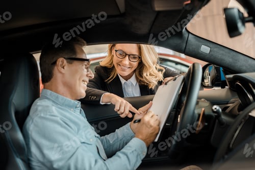 Preview: adult man signing contract with female car dealer while sitting in car