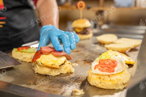Preview: Cook adding ingredients preparing hamburger on grill in restaurant kitchen