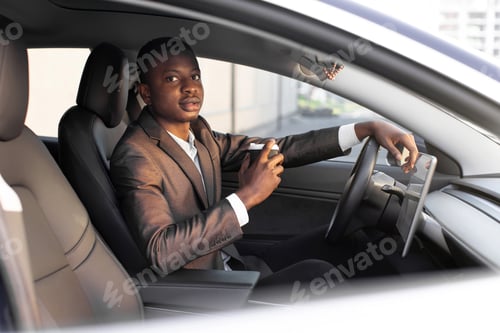Preview: Handsome young dark skinned man in formal wear sitting in his modern electric car