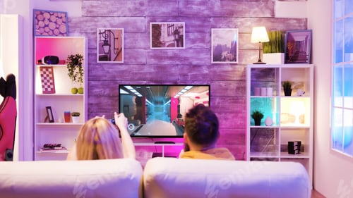 Preview: Good friends sitting on sofa and playing online shooter games