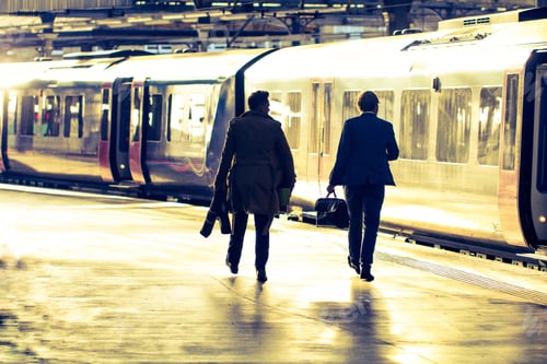 Preview: Two businessmen walking along a sunlit railway station platform before boarding a passenger train.