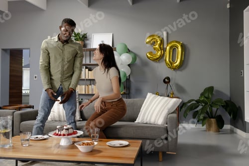 Preview: Celebrating 30th birthday, friends enjoying cake and snacks in modern living room