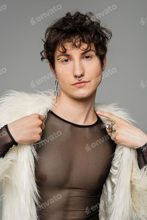Preview: trendy bigender person in white faux fur jacket and black transparent top looking at camera isolated