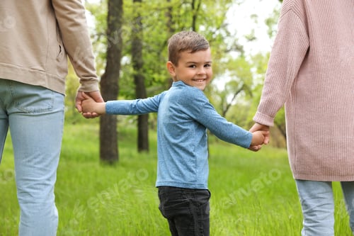 Preview: Happy little child holding hands with his parents in park. Family weekend