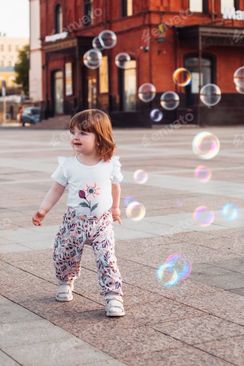 Preview: little girl playing fun with soap bubbles on the street in the city in summer at sunset