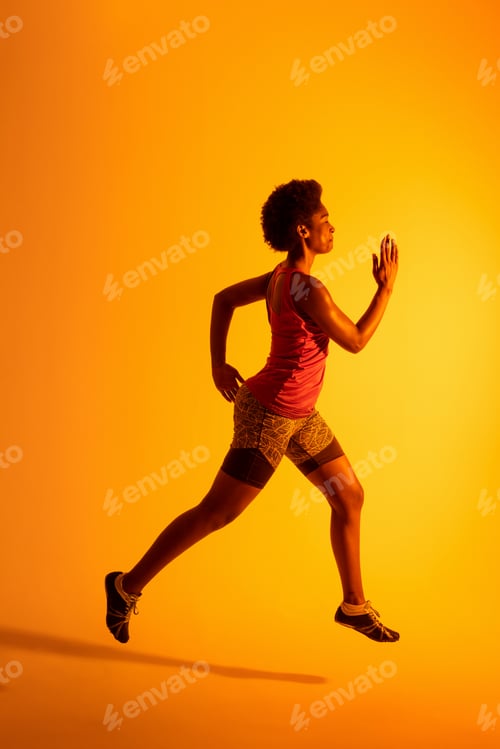 Preview: Vertical image of african american female athlete running in neon orange lighting