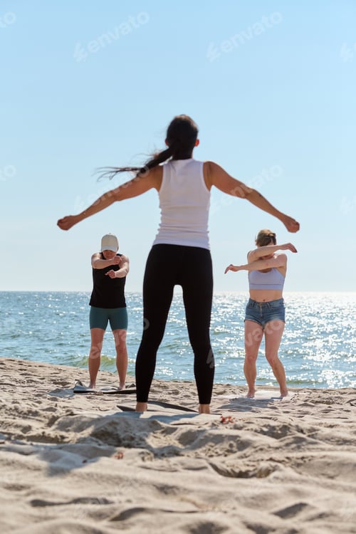 Preview: Group yoga session on Baltic Sea beach with stretching adults in morning light