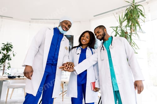 Preview: Group of three young African doctors, two men and woman, putting their hands together, standing in
