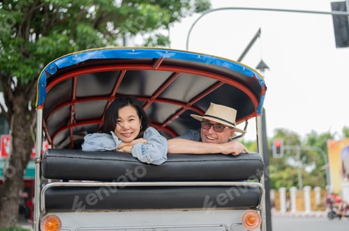Preview: Smiling white man and asian woman looking back while riding in tuk tuk three wheel taxi touring city