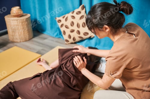 Preview: Masseuse making thai yoga massage. Woman therapist doing traditional massage treatment for patient.