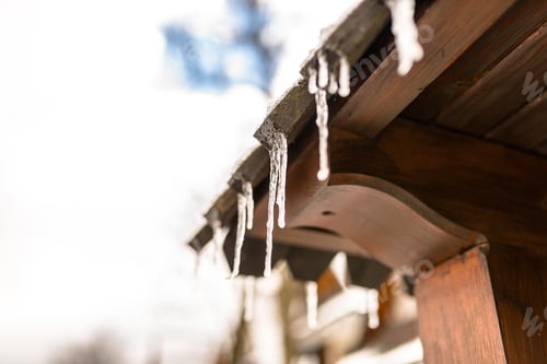Preview: Hanging icicles from the roof of a wooden building on a winter frosty day, a lot of snow on the roof