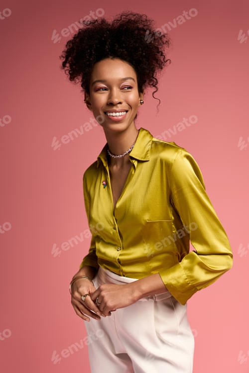 Preview: Joyful woman in vibrant shirt smiles against a soft pink background in a bright setting