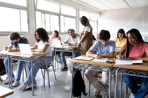 Preview: eacher helping teen male high school student with lesson. Classmates focused on the task at hand.