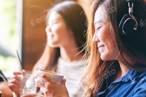Preview: A beautiful asian woman enjoy listening to music with headphone while drinking coffee with friends