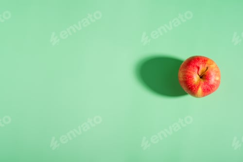 Preview: A vibrant red apple with a shadow on a green backdrop, displaying its natural beauty