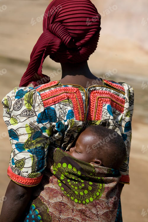 Preview: Woman in vibrant attire carrying a sleeping child