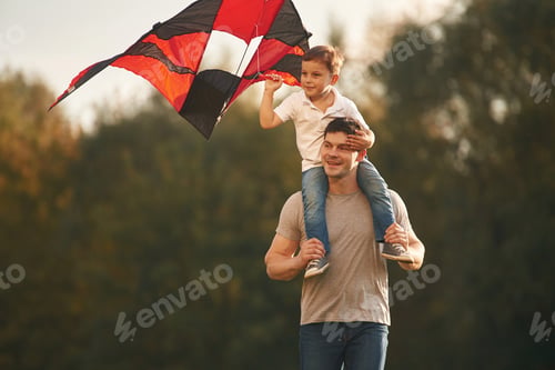 Preview: Red and black colored kite in hands. Father and little son are playing and having fun outdoors