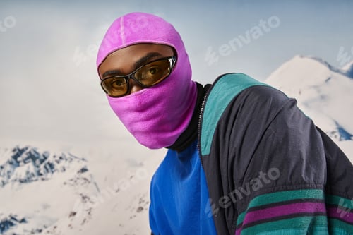 Preview: handsome stylish man wearing pink balaclava and sunglasses with snowy backdrop, winter concept