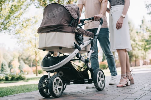 Preview: cropped image of mother and father walking with baby carriage in park