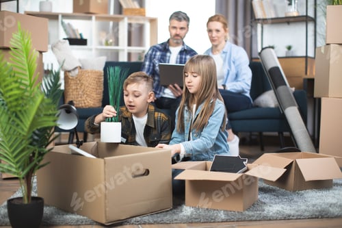 Preview: Parents sitting on sofa with laptop, while kids playing and unpacking boxes at new flat
