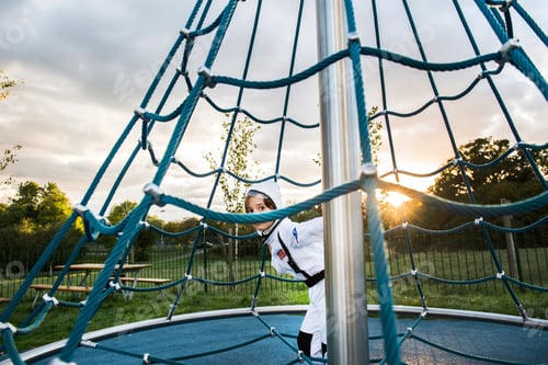 Preview: Portrait of boy in astronaut costume hiding and peering from playground climbing frame