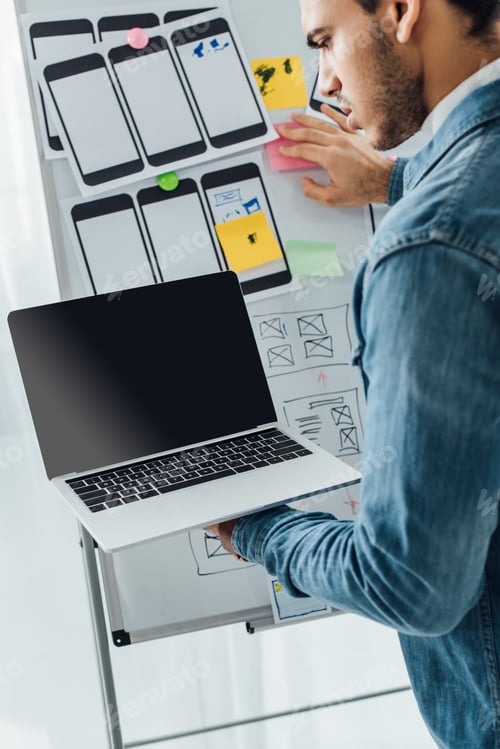 Preview: Ux designer using laptop near website templates on whiteboard in office