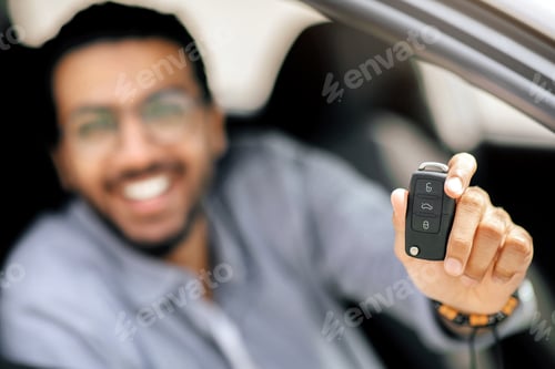 Preview: Blurred man showing car key at camera, closeup