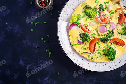 Preview: Omelette with broccoli, tomatoes and red onions on dark table.