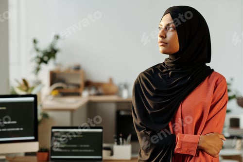 Preview: Young serious businesswoman in black hijab looking aside against workplace