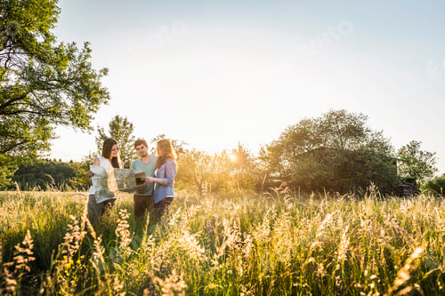 Preview: A group of friends enjoying a golden sunset while exploring with a map in a lush meadow.