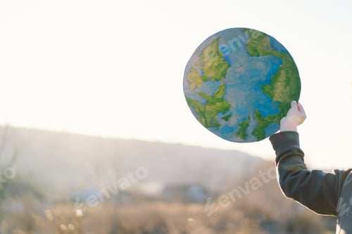 Preview: Little boy holding planet in hands against green spring background. Earth day