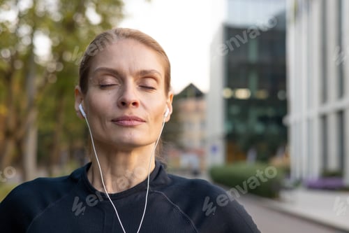 Preview: Sportswoman resting and breathing with headphones in an urban environment