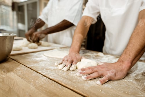 Preview: cropped shot of bakers kneading dough together at baking manufacture