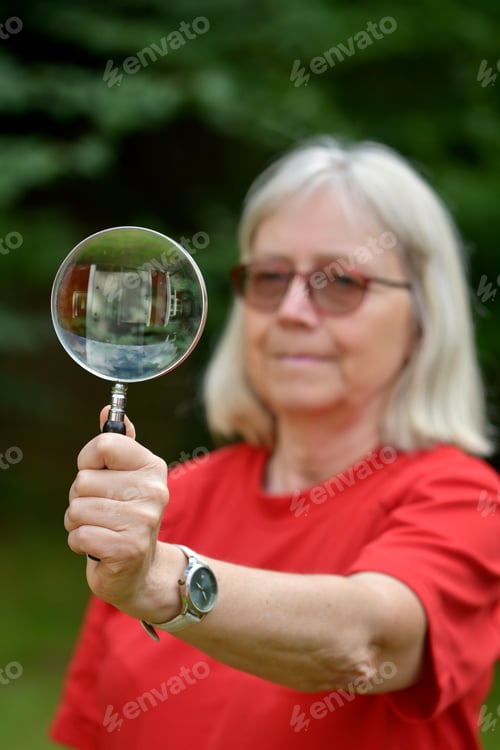 Preview: Funny portrait of senior woman wearing red tshirt and holding magnifying glass in front of her
