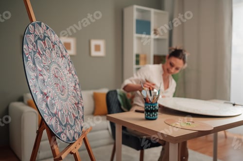 Preview: Female artist painting a mandala on a round canvas at home