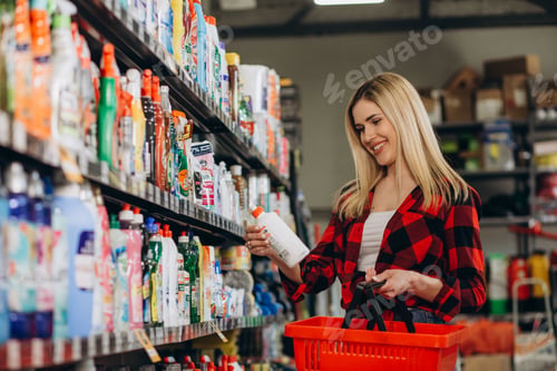 Preview: Interested young woman making purchases in household chemicals store, reading labels on bottles.