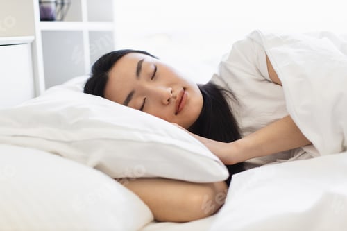 Preview: Asian woman peacefully sleeping in white bed in serene bedroom